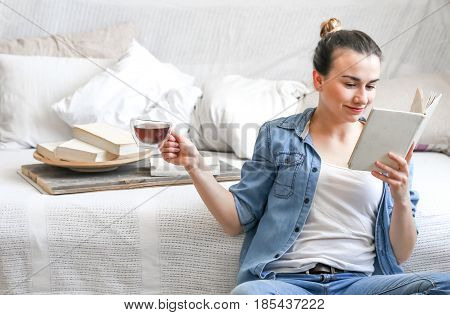 girl reading a book in a cozy room on the couch with a Cup of tea , the concept of leisure, and comfort