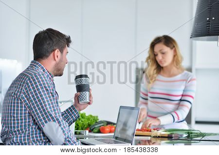 Couple standing and sitting at the kitchen while smiling and man reading a newspaper and holding mug before work