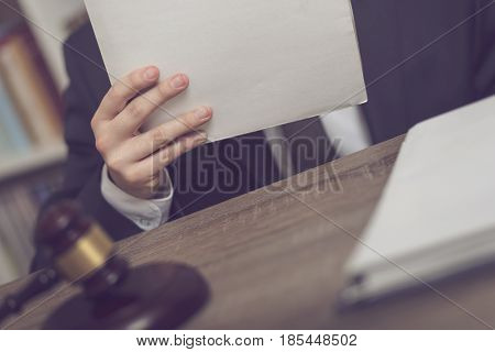 Detail of a judge sitting at his desk holding a file with a new case and studying it. Selective focus