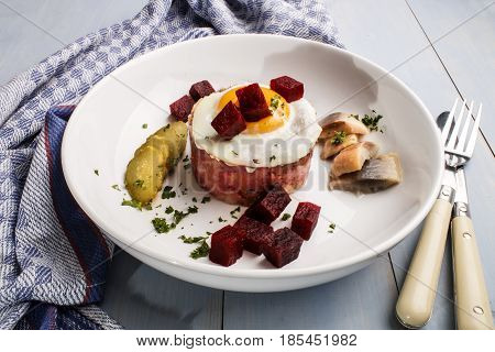 labskaus north german specialty made with potatoes beetroot sour herring gherkin slices fried egg and parsley on a fine dining plate