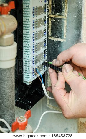 Man's hands inserts wires in a switch for thermostats and servo drives valves in a home heating system.