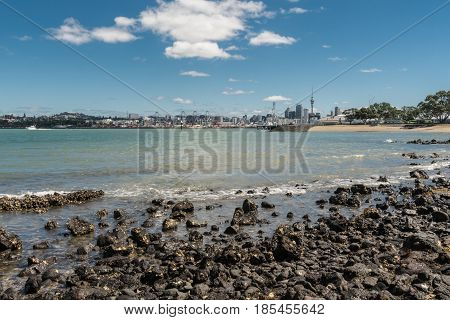 Auckland New Zealand - March 3 2017: City skyline with With commercial harbor and beyond seen over greenish ocean water under blue sky with some white clouds and shot from Devonport Beach.