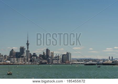 Auckland New Zealand - March 3 2017: City skyline with Westhaven and beyond seen over greenish ocean water under blue sky from Devonport boardwalk. Highrises Sky Tower airplane and boats.