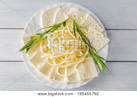 Soft cheese Chechil and Guda on plate with herbs on wooden table. Top view.
