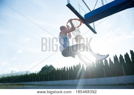 Young man jumping and making a fantastic slam dunk playing streetball, basketball. Urban authentic.