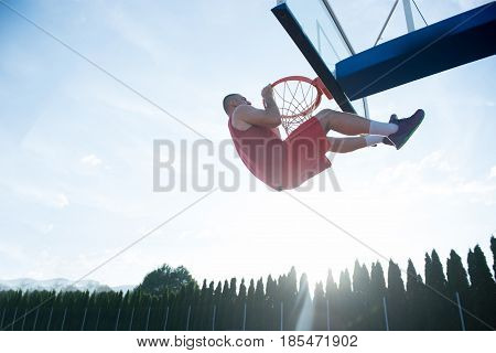 Young man jumping and making a fantastic slam dunk playing streetball, basketball. Urban authentic.