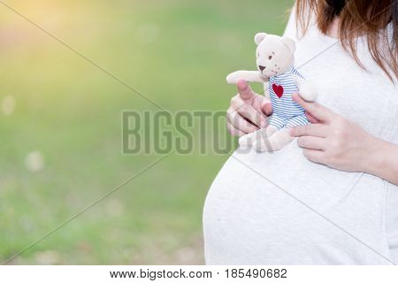 beautiful and happy pregnant asian woman in the garden with doll