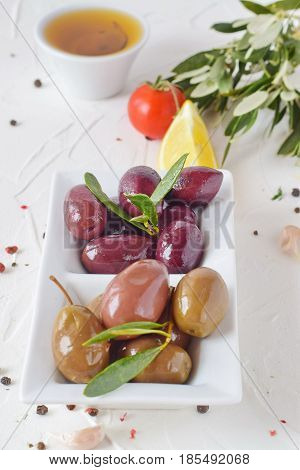White plate with black and green olives with olive leaves on a white abstract background with lemon, cherry tomato, spices. Healthy food. Greek food. Mediterranean food