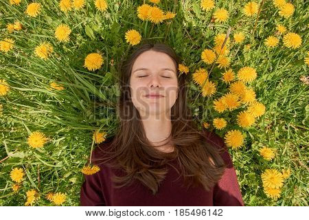 Beautiful young woman relaxing on a meadow with many dandelions in the spring sun. Lying between dandelions.