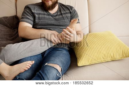 Two young people relaxing on sofa. Man massaging woman's feet.