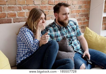 Young woman and man sitting on sofa and watching tv.
