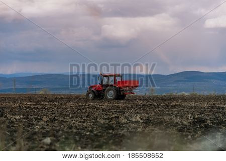 Tractor spreading artificial fertilizers in spring days