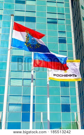 Samara Russia - May 7 2017: Flags of Samara region Russia and oil company Rosneft fluttering against the office building of the OJSC Samaraneftegaz
