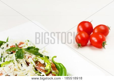 Traditional classic Shopska salad with tomatoes, peppers, cucumbers and cheese in white dish on white wooden table. Bulgarian cuisine, Balkan culture