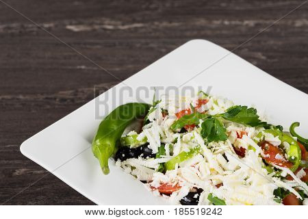 Traditional classic Shopska salad with tomatoes, peppers, cucumbers and cheese in white dish on grey wooden table. Bulgarian cuisine, Balkan culture