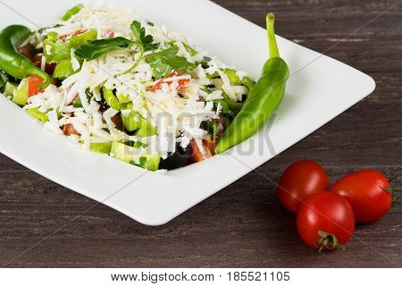 Traditional classic Shopska salad with tomatoes, peppers, cucumbers and cheese in white dish on grey wooden table. Bulgarian cuisine, Balkan culture