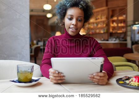 Young African American Woman In Bright Casual Turtleneck Spending Free Time In Coffee House Sitting