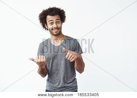 Young cheerful african man pointing fingers in side over white background. Copy space.