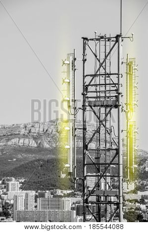 Aerial view of telecommunication tower with multiple antennas and data transmitters with light radio waves emission and with beautiful city in the background and wide mountain area
