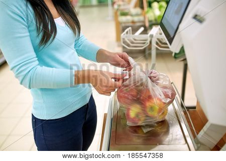 shopping, sale, consumerism and people concept - woman weighing apples on scale at grocery store