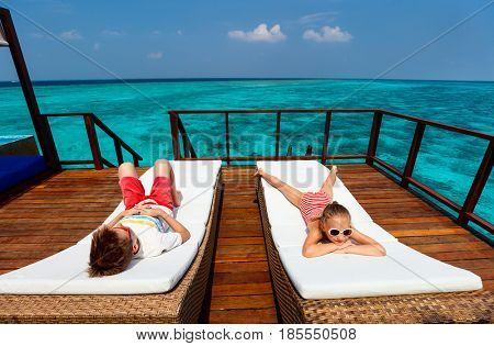 Kids enjoying tropical summer vacation relaxing at overwater villa in luxury resport