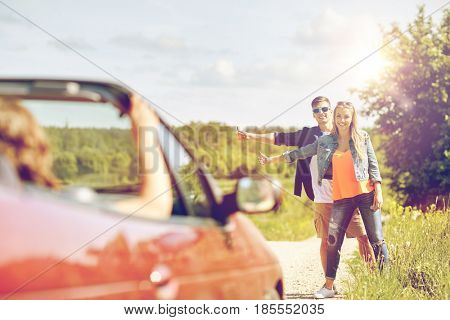 road trip, hitchhike, travel, gesture and people concept - happy couple hitchhiking and stopping car at countryside road