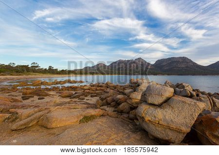 Rocky coastline on Freycinet national park beach in the evening. Big granite rocks during sunset with view of Hazards mountain range from Coles Bay. East coast of Tasmania, Australia