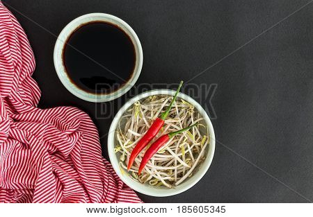 Red chili peppers on soybean sprouts in green bowl soy sauce in bowl and a striped towel on black background. Asian food concept.