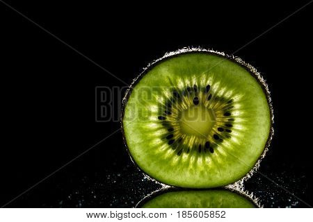 Healthy sliced kiwi fruit backlit on black backgroud close up with reflection