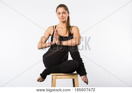 Feel relaxed. Young pleasant woman sitting in lotus pose on chair with closed eyes and putting her palms together