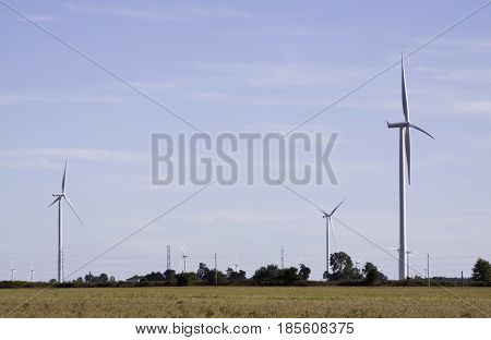 Close landscape view of multiple wind turbines in a farmer's field near Windsor, Ontario with the moon visible on a sunny late afternoon in September.