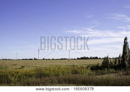 Wide landscape of multiple wind turbines in a farmer's field near Windsor, Ontario with the moon visible on a sunny late afternoon in September.