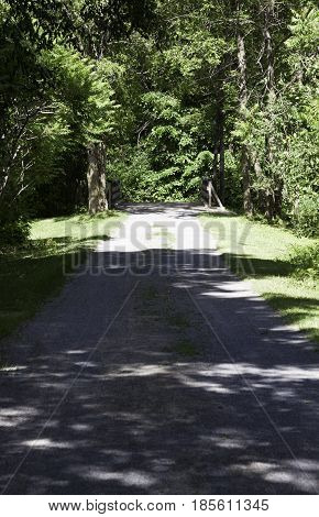 Vertical of a gravel walking path through the trees and foliage in Notre Dame de Ile Perrot, Quebec on a sunny day in June.