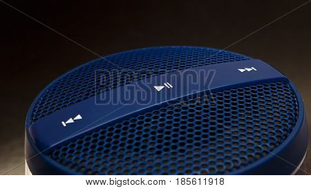 Blue speaker with control buttons play pause next previous track on dark background