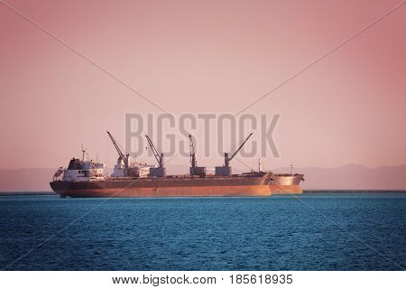 Two bulk carriers with cranes loading cargo at sunset off the coast of Long Beach, California