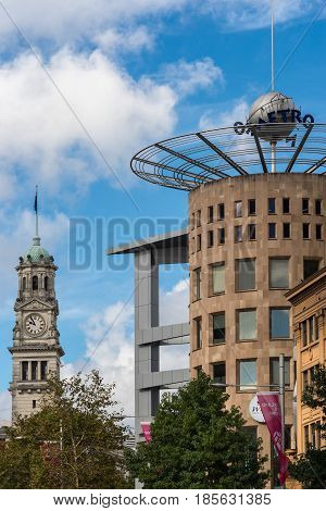 Auckland New Zealand - March 4 2017: The brown stone tower of the Metro complex office and shopping building under blue sky with white clouds. Town Hall Clock Tower in photo with green vegetation.
