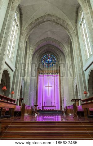 Auckland New Zealand - March 4 2017: Chancel at old part of Holy Trinity Cathedral features wooden benches and altar in front of purple lighted back with large cross. Towering ceiling.