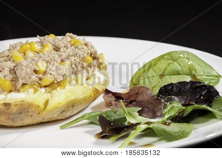 Healthy tuna sweetcorn baked potato meal with side baby leaf salad and dressing. Served on a white plate in close up against black background. Nutritional low calorie food.
