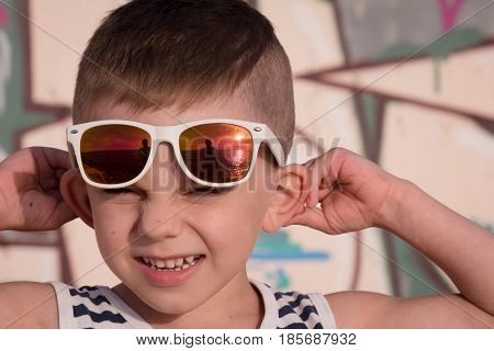 portrait of cute little boy wearing striped shirt and white sunglasses with reflections of photographer and sea sunset
