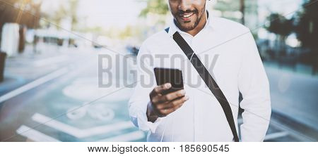 Happy american African man using smartphone outdoor.Portrait of young black cheerful man texting a sms message while listining to music.Blurred background, horizontal wide.Flare effects