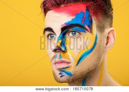 portrait of young attractive man with colored face paint on a yellow background. Professional Makeup Fashion. fantasy art makeup