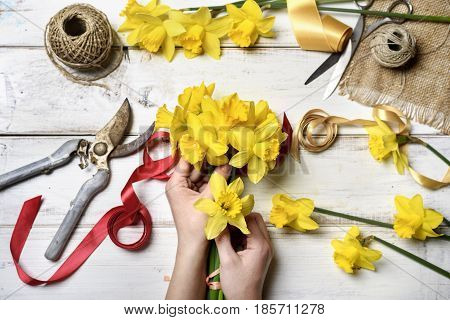 Woman making bouquet of narcissus. top view of hands holding flower arrangement