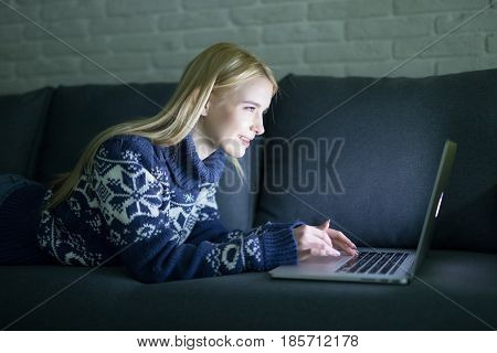 Happy Woman Lying On The Sofa With Her Laptop At Night At Home In The Sitting Room