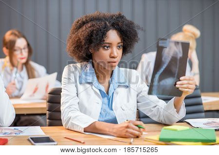 Multi ethnic group of medical students in uniform working on medical research sitting at the desk with x-ray and books in the modern classroom