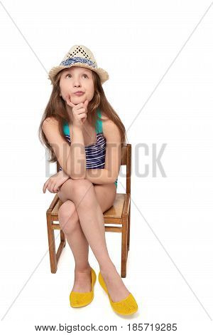 Full length child girl in swimsuit and summer hat sitting on wooden chair thinking contemplating looking up at blank copy space, studio portrait