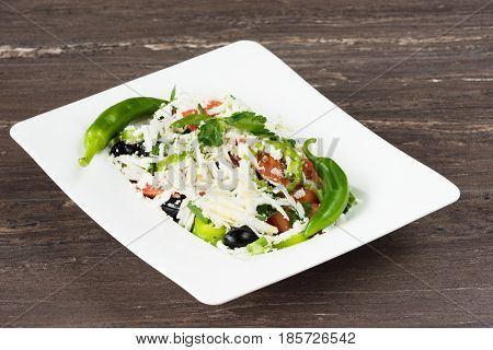 Traditional classic Shopska salad with tomatoes, peppers, cucumbers and cheese in white dish on grey wooden table. Bulgarian cuisine, Balkan culture