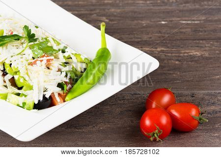 Traditional classic Shopska salad with tomatoes, peppers, cucumbers and cheese in white dish on grey wooden table. Bulgarian cuisine, Balkan culture