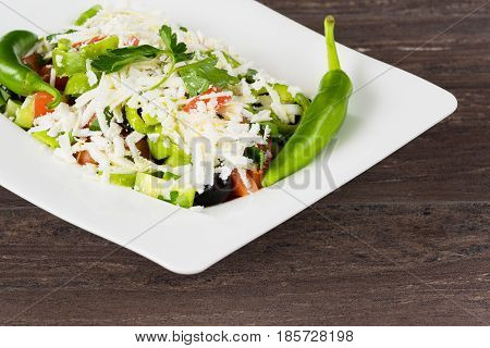 Traditional classic Shopska salad with tomatoes, peppers, cucumbers and cheese in white dish on grey wooden table. Bulgarian cuisine, Balkan culture