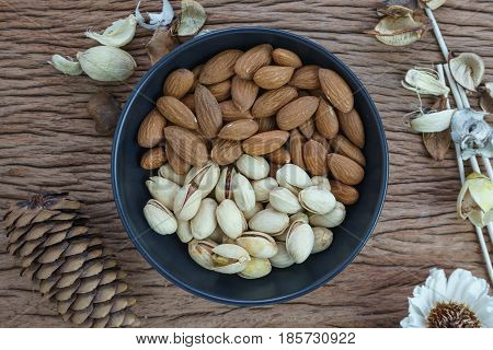 Roasted healthy delicious pistachios and almonds nuts food in black bowl on wooden table background.