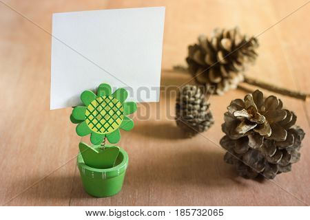 Small stand with blank white card and dry pine flower on wood background.